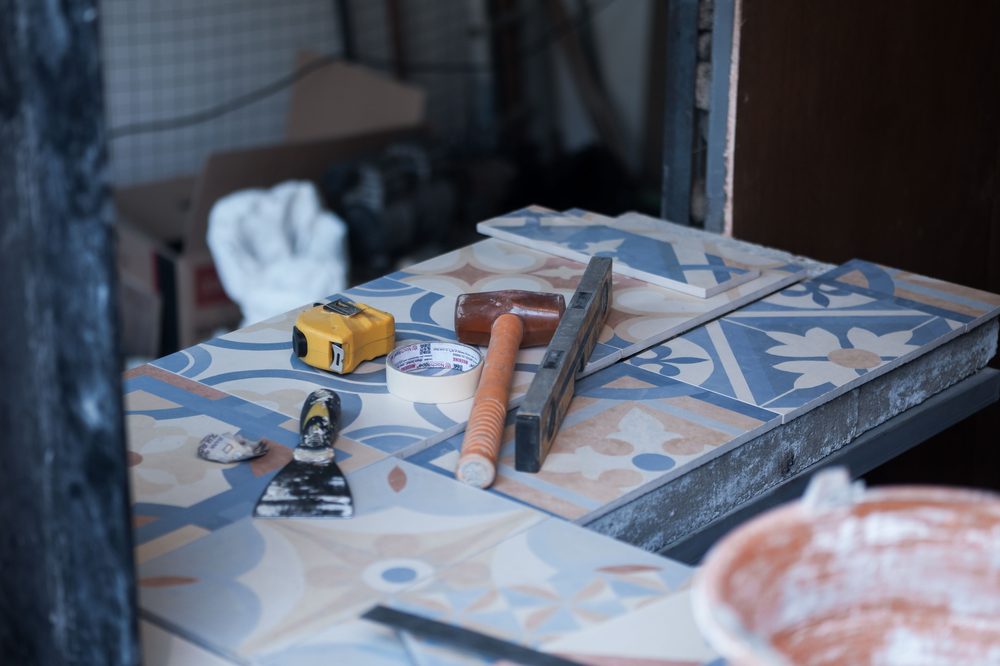 Maillet, niveau, spatule et seau de colle posés sur des carreaux de ciment à motifs